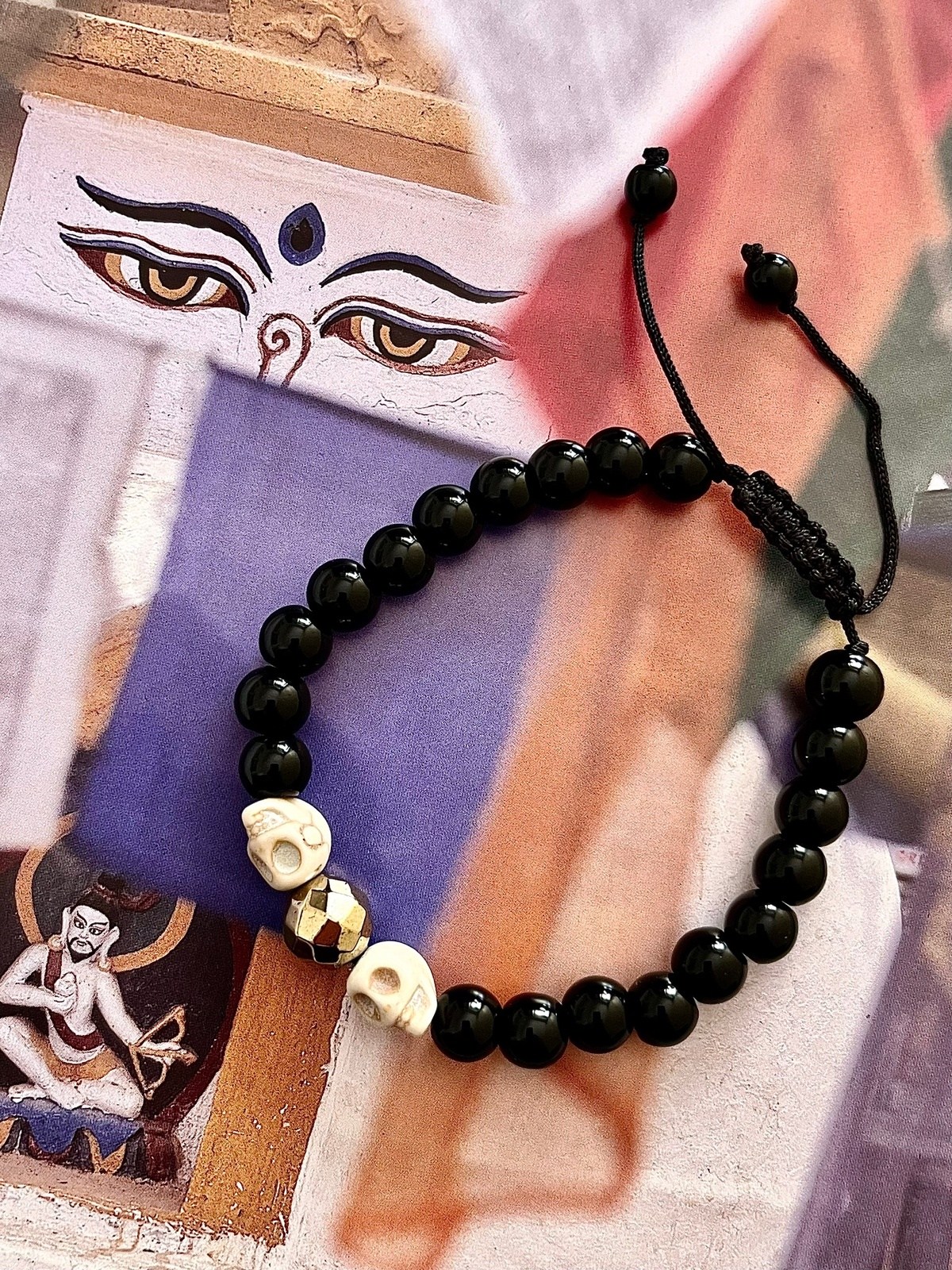 spark of life unisex adjustable bracelet with black onyx beads, two white howlite skulls, and golden faceted hematite beads