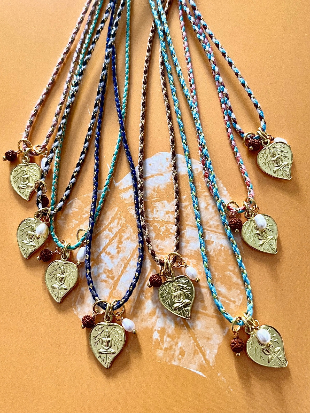 buddha bodhi magic cord necklace with a golden thai pendant shaped like a heart and bodhi tree leaf, delicately depicting the buddha in meditation, held by a colorful golden cord