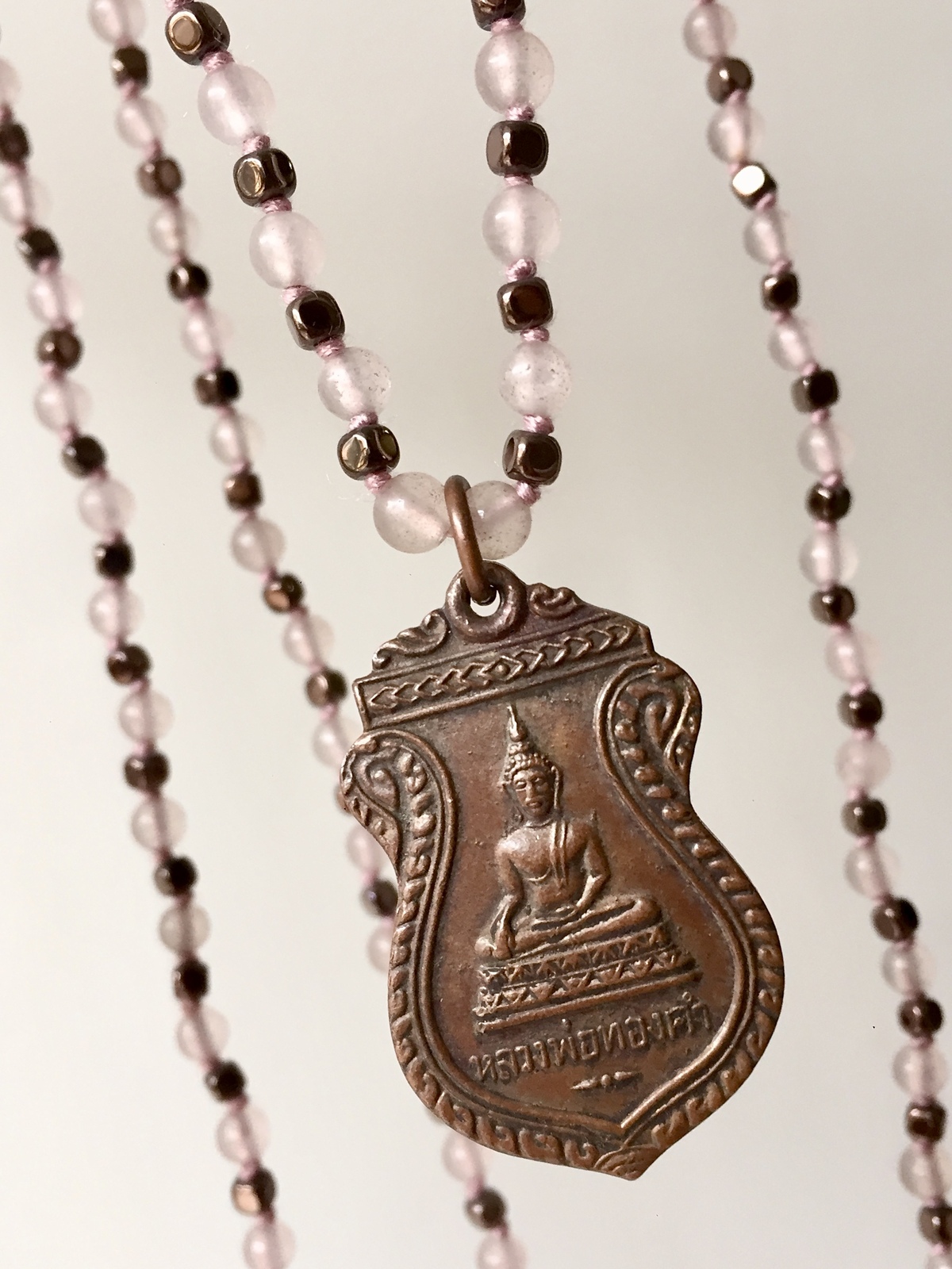 buddha grace necklace handcrafted with soft rose quartz beads and faceted bronze hematite, featuring a thai buddhist copper amulet with a serene seated buddha, symbolizing love, compassion, and mindfulness