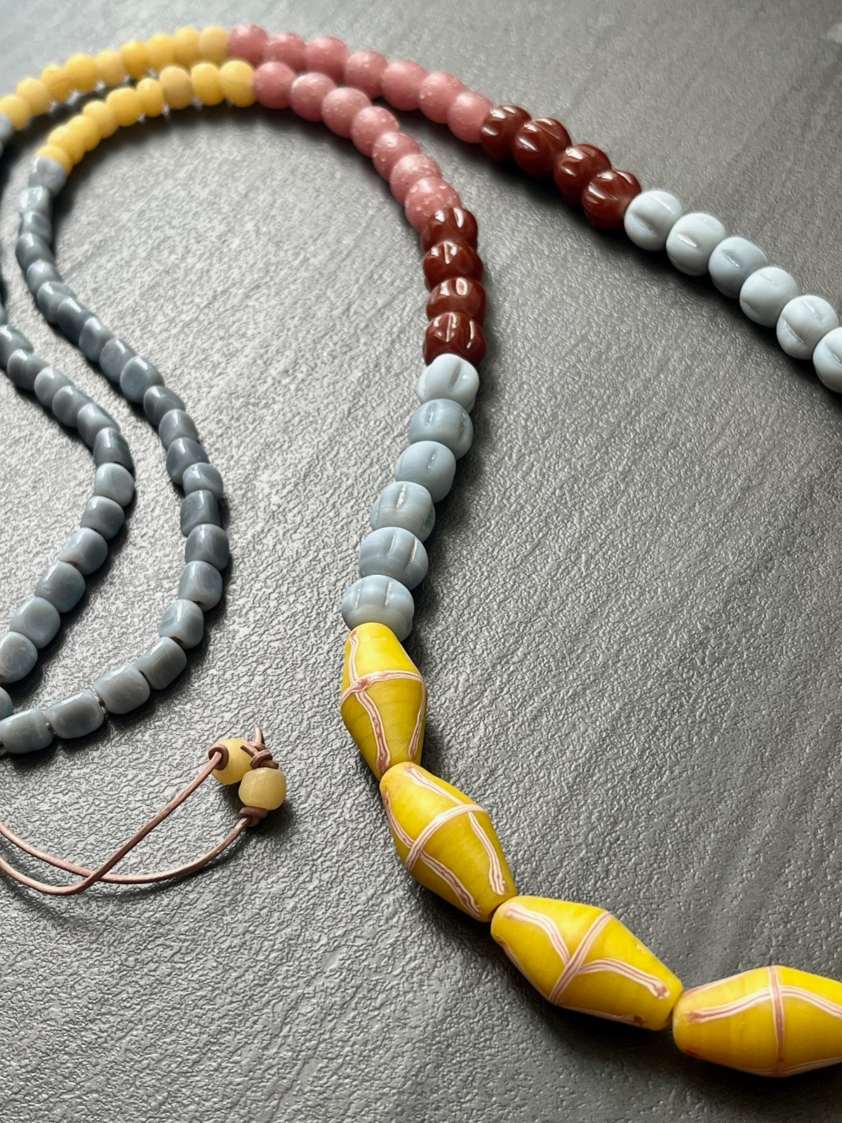 java necklace with bright yellow, pink and grey handmade javanese glass beads in different shapes on a leather strap inspired by indonesian textiles