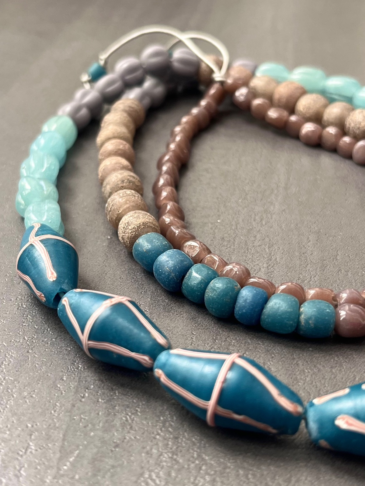 java necklace with peacock blue, aqua and brown handmade javanese glass beads in different shapes on a leather strap inspired by indonesian textiles