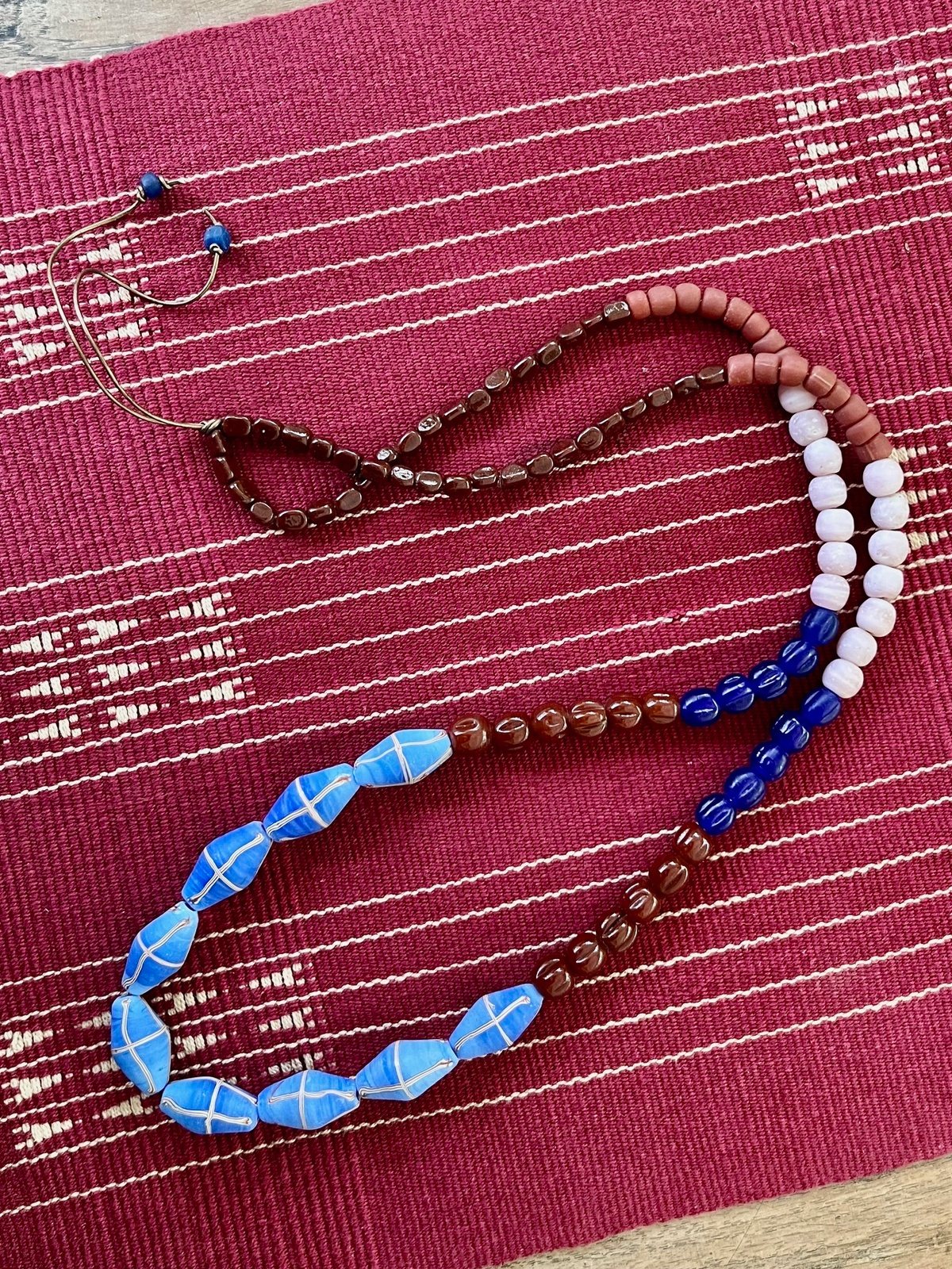 java necklace with sky blue, brown, and rose handmade javanese glass beads in different shapes on a leather strap inspired by indonesian textiles