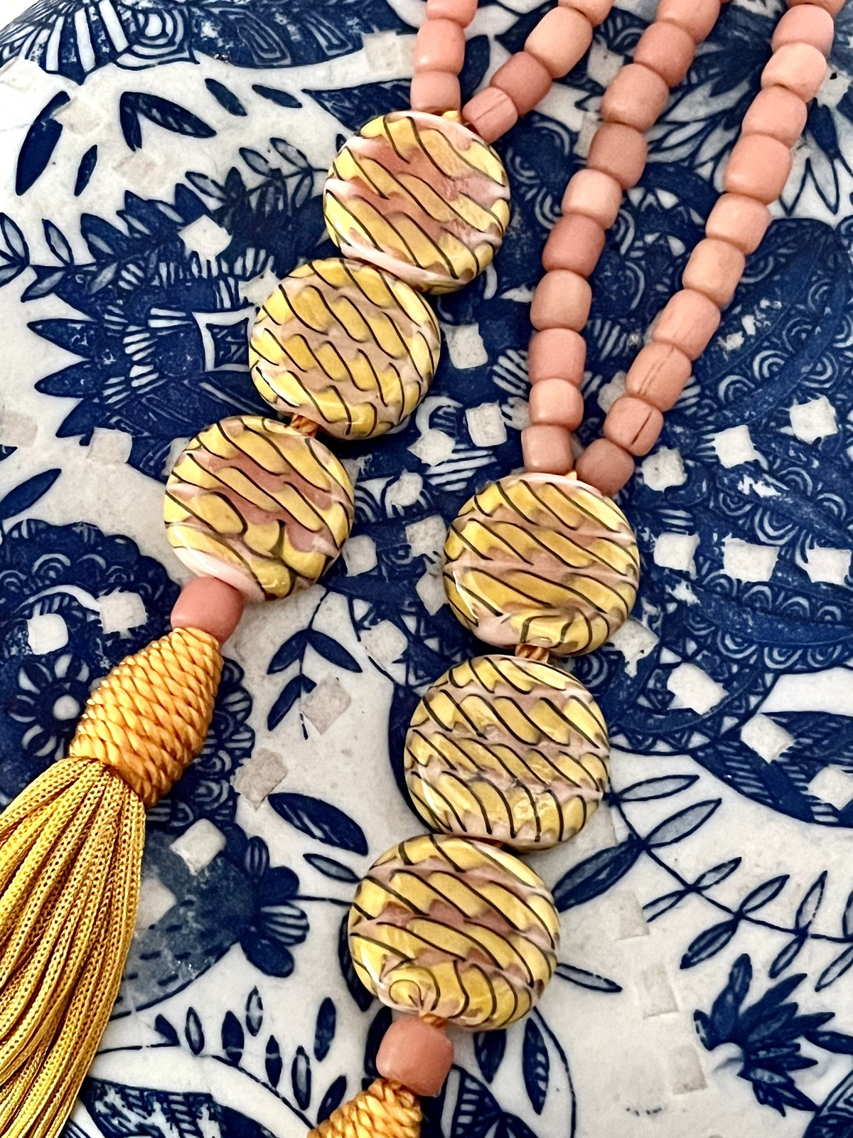 sarong necklace inspired by balinese sarongs, handmade with pink javanese matte glass beads, three glossy multicolor beads, and a matching viscose yellow tassel.
