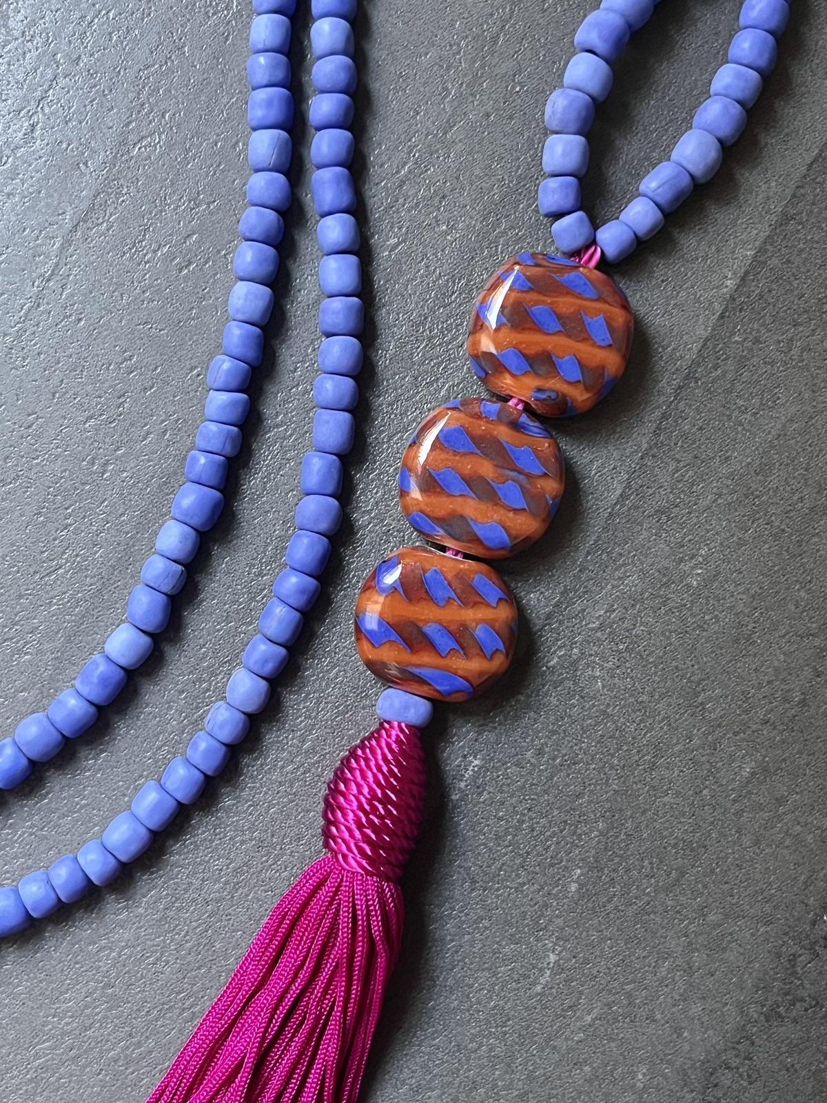 sarong necklace inspired by balinese sarongs, handmade with sky blue javanese matte glass beads, three glossy multicolor beads, and a matching viscose fuchsia tassel.