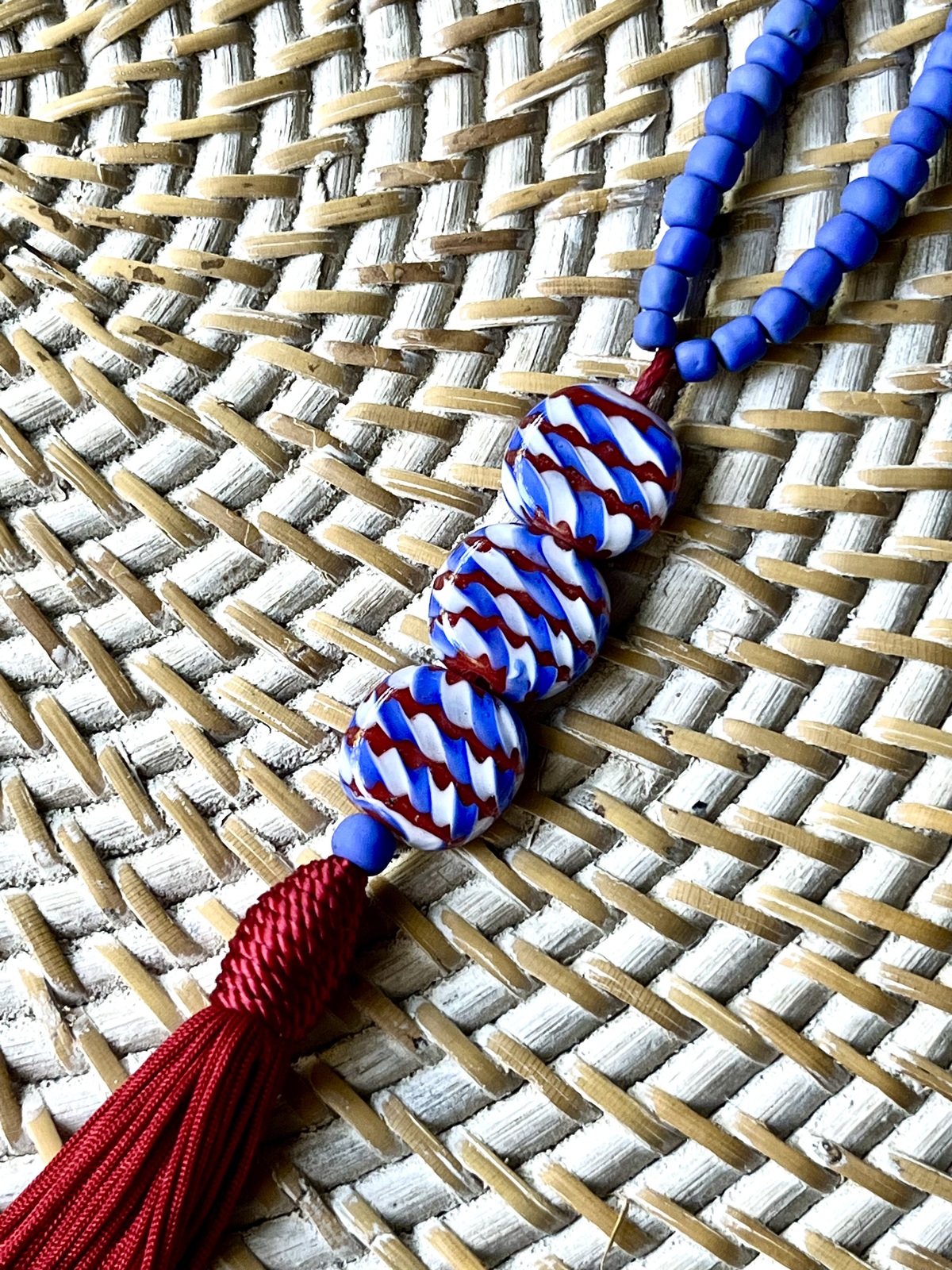sarong necklace inspired by balinese sarongs, handmade with sky blue javanese matte glass beads, three glossy multicolor beads, and a matching viscose red tassel