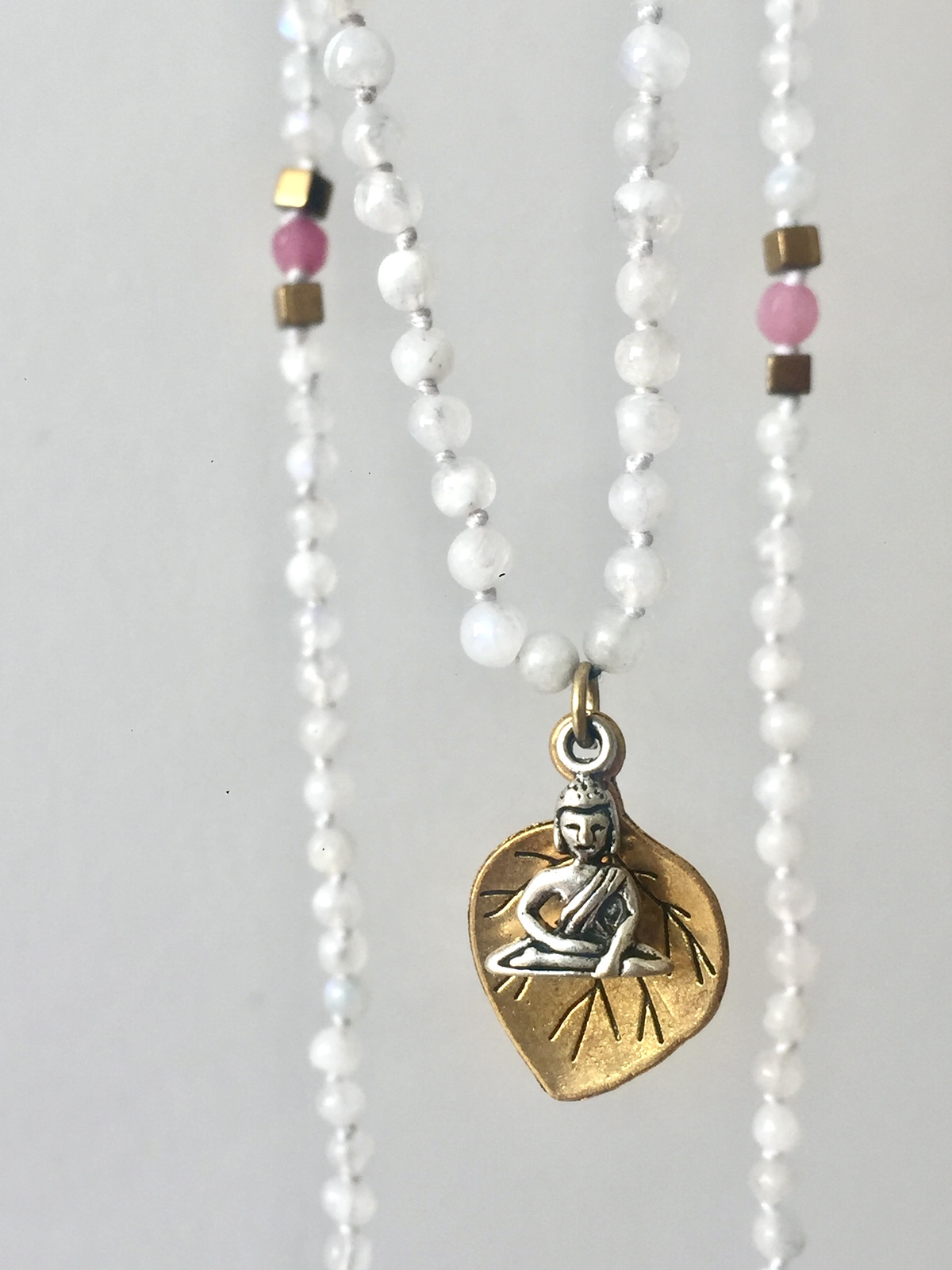 under the bodhi tree necklace with hand-knotted white moonstone beads, golden hematite accents, a pink agate bead, featuring a golden bodhi tree leaf and a tiny silver buddha pendant seated in meditation