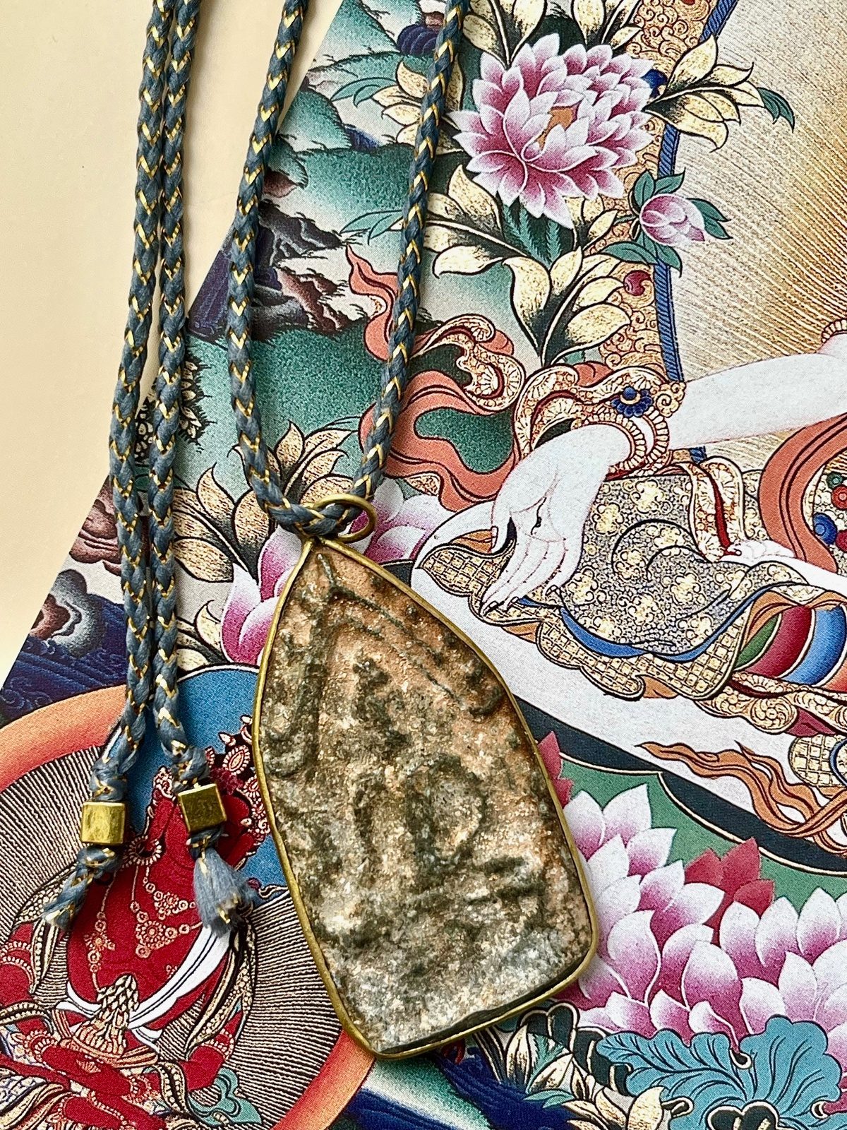 necklace with grey blue golden lurex cotton cord and a thai clay amulet depicting the buddha in meditation, symbolizing protection, grounding, and spiritual connection