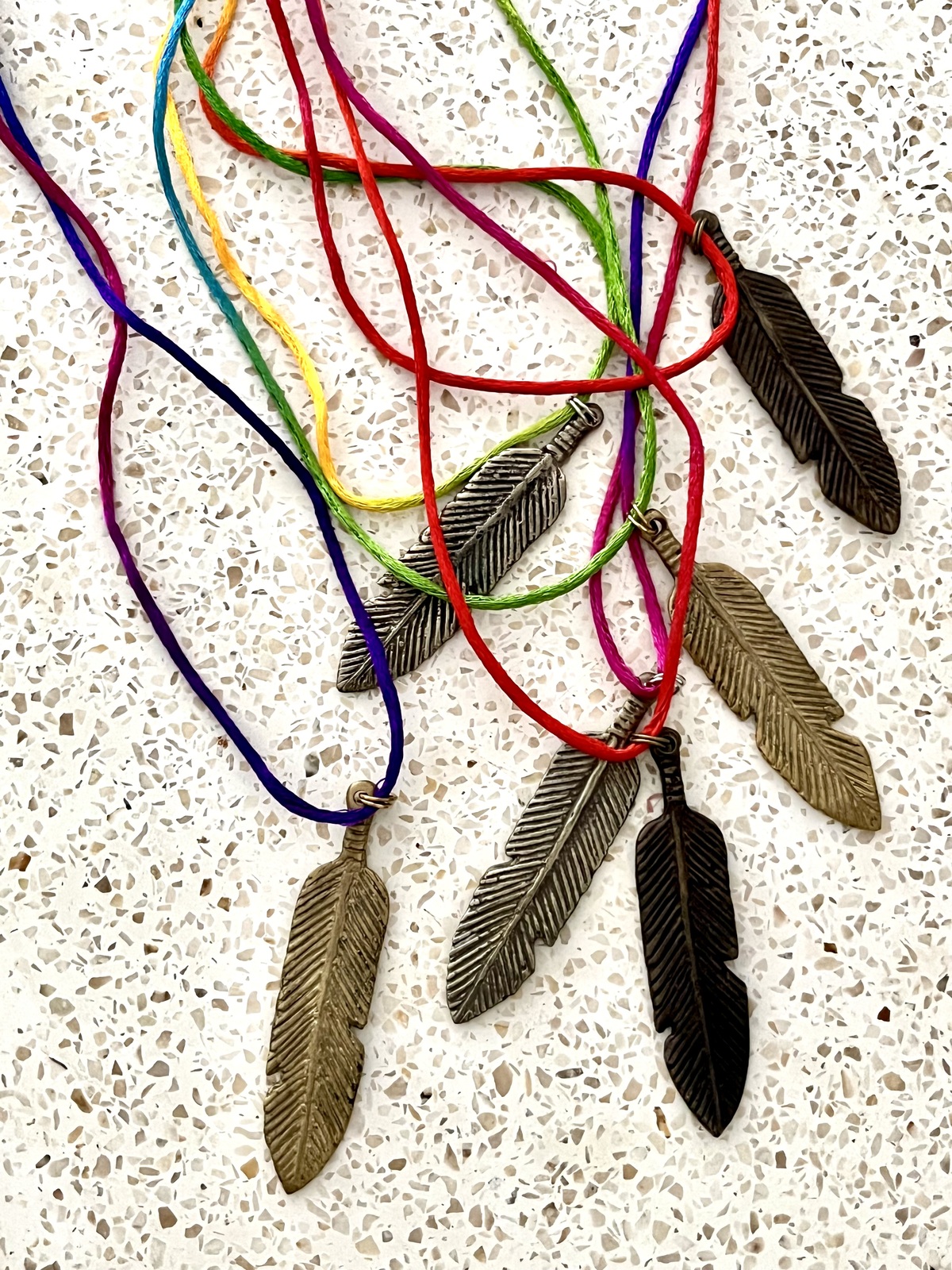 necklace with rainbow-colored indian mouli cord and brass feather pendant in gold, bronze, or silver finish, symbolizing freedom, protection, and spiritual connection