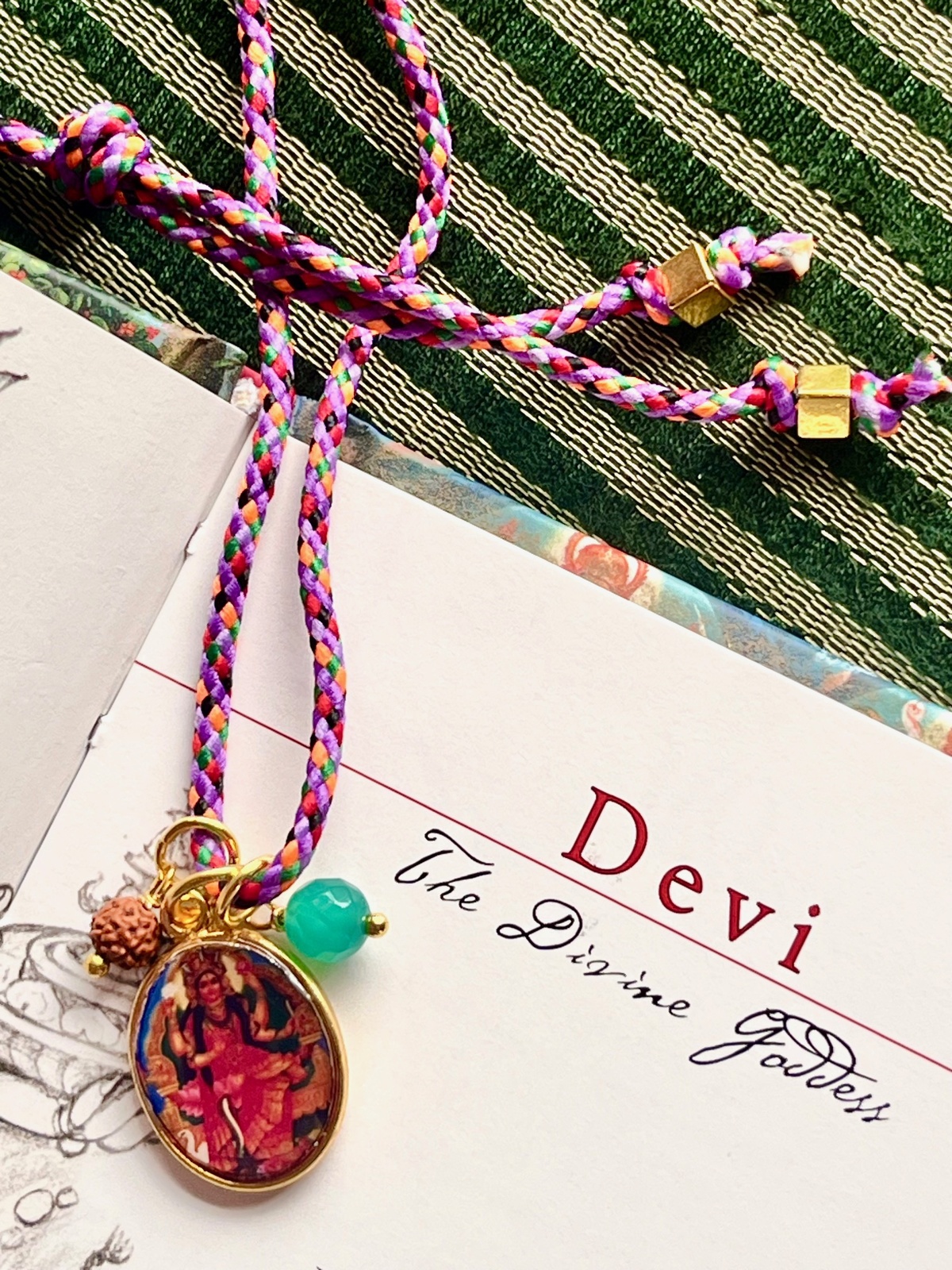 colorful kali funky cord necklace with adjustable purple pop cord, vintage golden pendant of goddess kali, rudraksha seed, and agate bead, a vibrant accessory symbolizing transformation, liberation, and protection