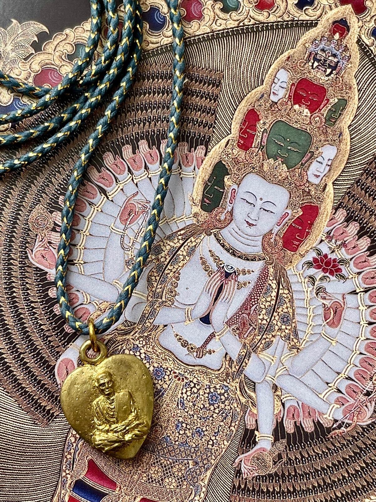 necklace with grey blue golden lurex cotton cord and thai brass amulet showing a heart holding a buddhist monk, symbolizing compassion, protection, and spiritual guidance