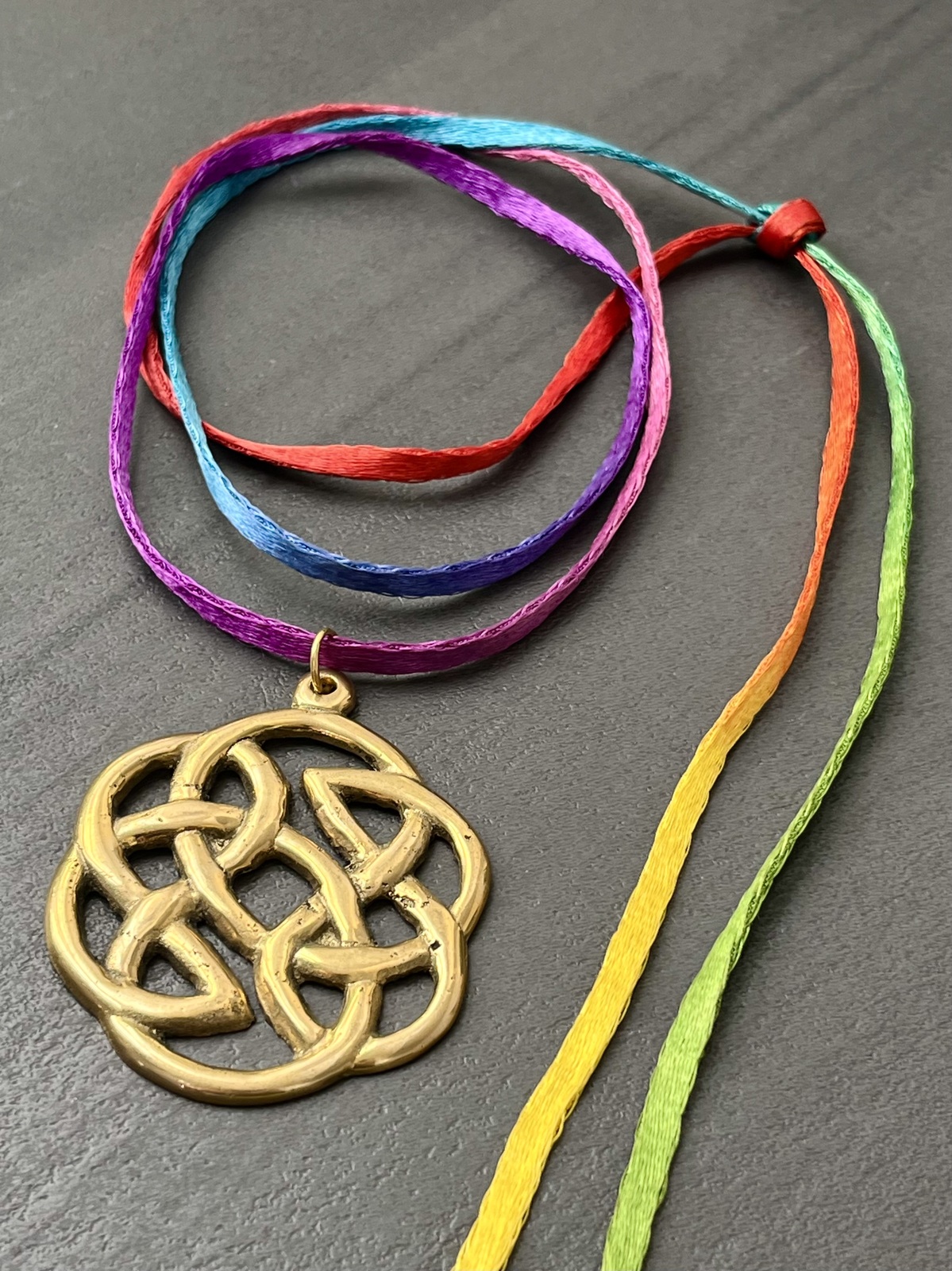 necklace with rainbow-colored indian mouli cord and golden brass eternity knot pendant, symbolizing unity, protection, and harmony