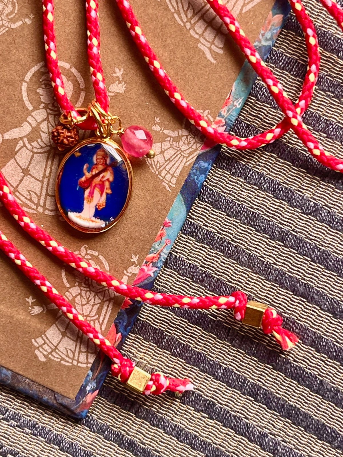colorful sarasvati funky cord necklace with adjustable red pop cord, vintage golden pendant of goddess sarasvati, rudraksha seed, and agate bead, a vibrant accessory symbolizing wisdom, knowledge, and creative inspiration